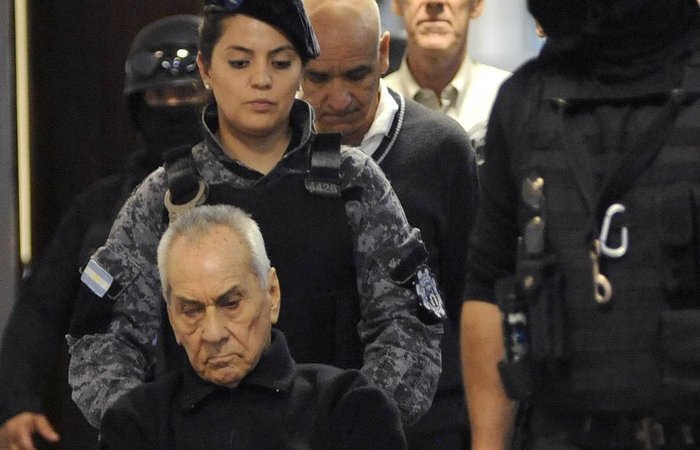 Padres Nicola Corradi (na cadeira de rodas) e Horacio Corbacho (ao fundo, de branco) e ex-jardineiro do Instituto Pr&oacute;volo Armando Gomez (centro, de su&eacute;ter preto) s&atilde;o escoltados at&eacute; o julgamento em Mendoza, Argentina./Foto: Andres Larrovere/AFP