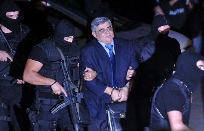 Golden Dawn Nikos Michaloliakos, líder do partido neonazista grego, é escoltado por uma polícia mascarada a um tribunal de Atenas. Registro de 2013/Foto: Louisa Gouliamaki/AFP Golden Dawn Nikos Michaloliakos, líder do partido neonazista grego, é escoltado por uma polícia mascarada a um tribunal de Atenas. Registro de 2013/Foto: Louisa Gouliamaki/AFP