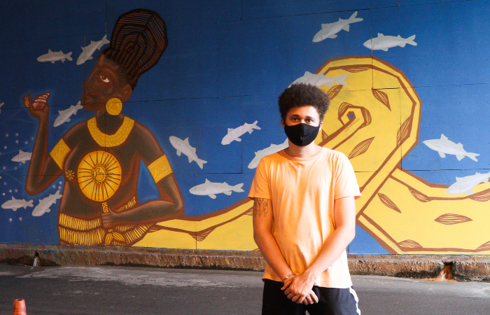 Emerson Crazy traz ancestralidade e vivência com a fé em painel composto por dois homens ao centro de uma floresta com fundo dourado