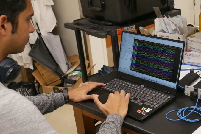 No laboratório, Duke University Ph.D. o candidato Kumar Duraivel analisa um conjunto colorido de dados de ondas cerebrais. Cada matiz e linha exclusivos representam a atividade de um dos 256 sensores, todos registrados em tempo real no cérebro de um paciente na sala de cirurgia/foto: Dan Vahaba/Duke University/Divulgação No laboratório, Duke University Ph.D. o candidato Kumar Duraivel analisa um conjunto colorido de dados de ondas cerebrais. Cada matiz e linha exclusivos representam a atividade de um dos 256 sensores, todos registrados em tempo real no cérebro de um paciente na sala de cirurgia/foto: Dan Vahaba/Duke University/Divulgação
