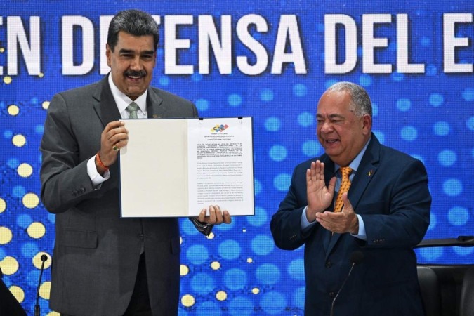 Nicolás Maduro (E) mostra a ata com o resultado da consulta popular de domingo, aplaudido pelo presidente do Conselho Nacional Eleitoral, Elvis Amoroso/Crédito: Federico Parra/AFP Nicolás Maduro (E) mostra a ata com o resultado da consulta popular de domingo, aplaudido pelo presidente do Conselho Nacional Eleitoral, Elvis Amoroso/Crédito: Federico Parra/AFP