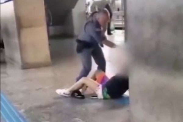 Homem fardado agredindo jovem caída no chão/Crédito: Reprodução/Instagram Homem fardado agredindo jovem caída no chão/Crédito: Reprodução/Instagram