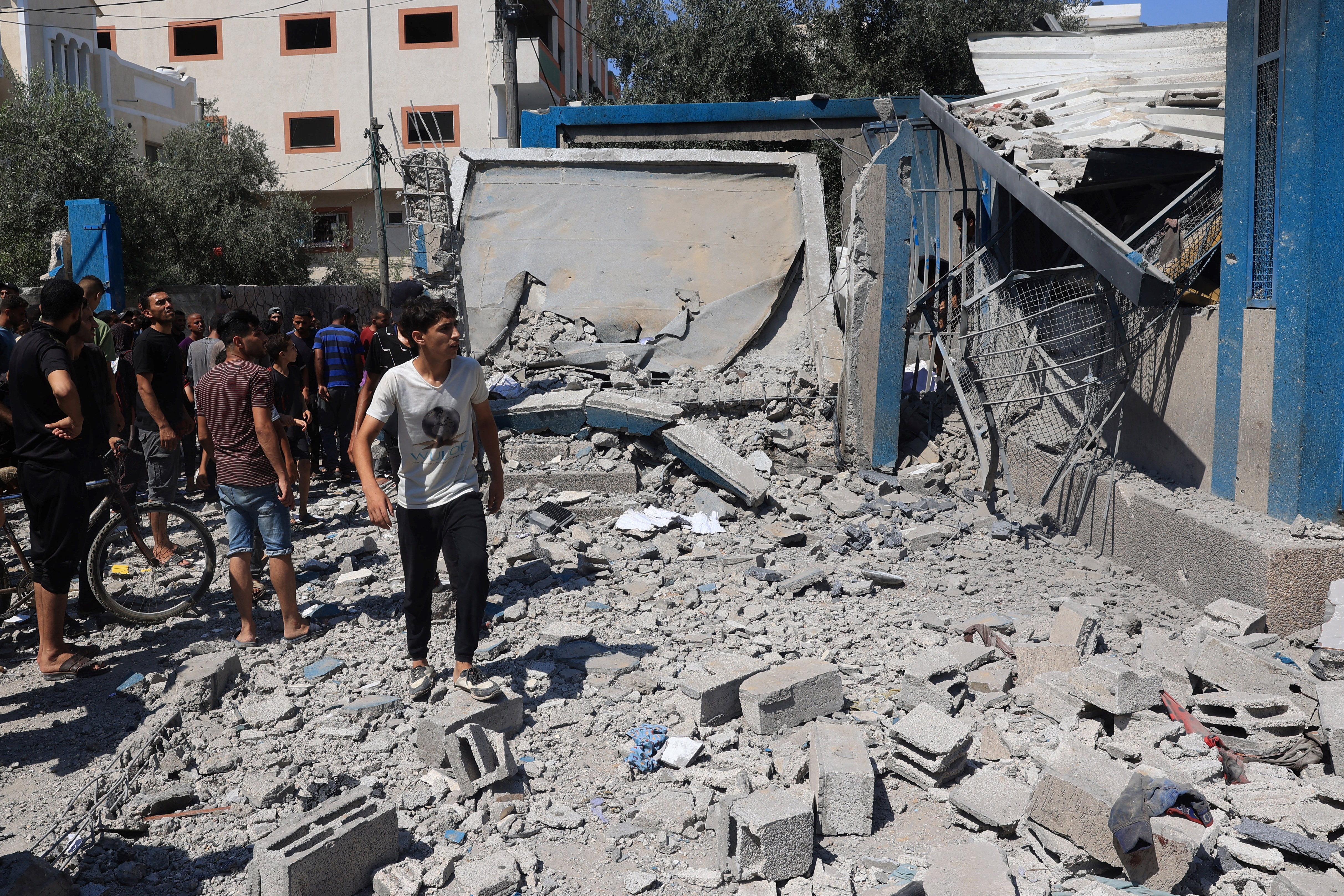 Homem palestino caminha sobre os escombros enquanto outros avaliam os danos após o bombardeio militar israelense da UNRWA, que administra a escola de Abu Araban, transformada em abrigo, no campo de refugiados de Nuseirat/Foto: EYAD BABA / AFP Homem palestino caminha sobre os escombros enquanto outros avaliam os danos após o bombardeio militar israelense da UNRWA, que administra a escola de Abu Araban, transformada em abrigo, no campo de refugiados de Nuseirat/Foto: EYAD BABA / AFP