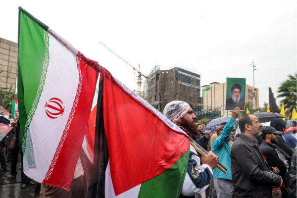 Um homem fica na chuva com uma bandeira iraniana e uma palestina durante um protesto anti-Israel na Praça Palestina, em Teerã/Crédito: ATTA KENARE / AFP Um homem fica na chuva com uma bandeira iraniana e uma palestina durante um protesto anti-Israel na Praça Palestina, em Teerã/Crédito: ATTA KENARE / AFP