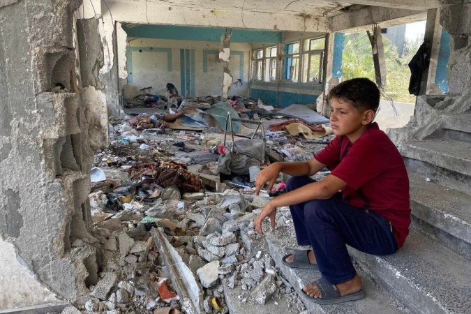 Menino sentado nos escombros de uma escola destruída da UNRWA em Nuseirat, área central da Faixa de Gaza/foto: Reproduzido com permissão da UNRWA Menino sentado nos escombros de uma escola destruída da UNRWA em Nuseirat, área central da Faixa de Gaza/foto: Reproduzido com permissão da UNRWA