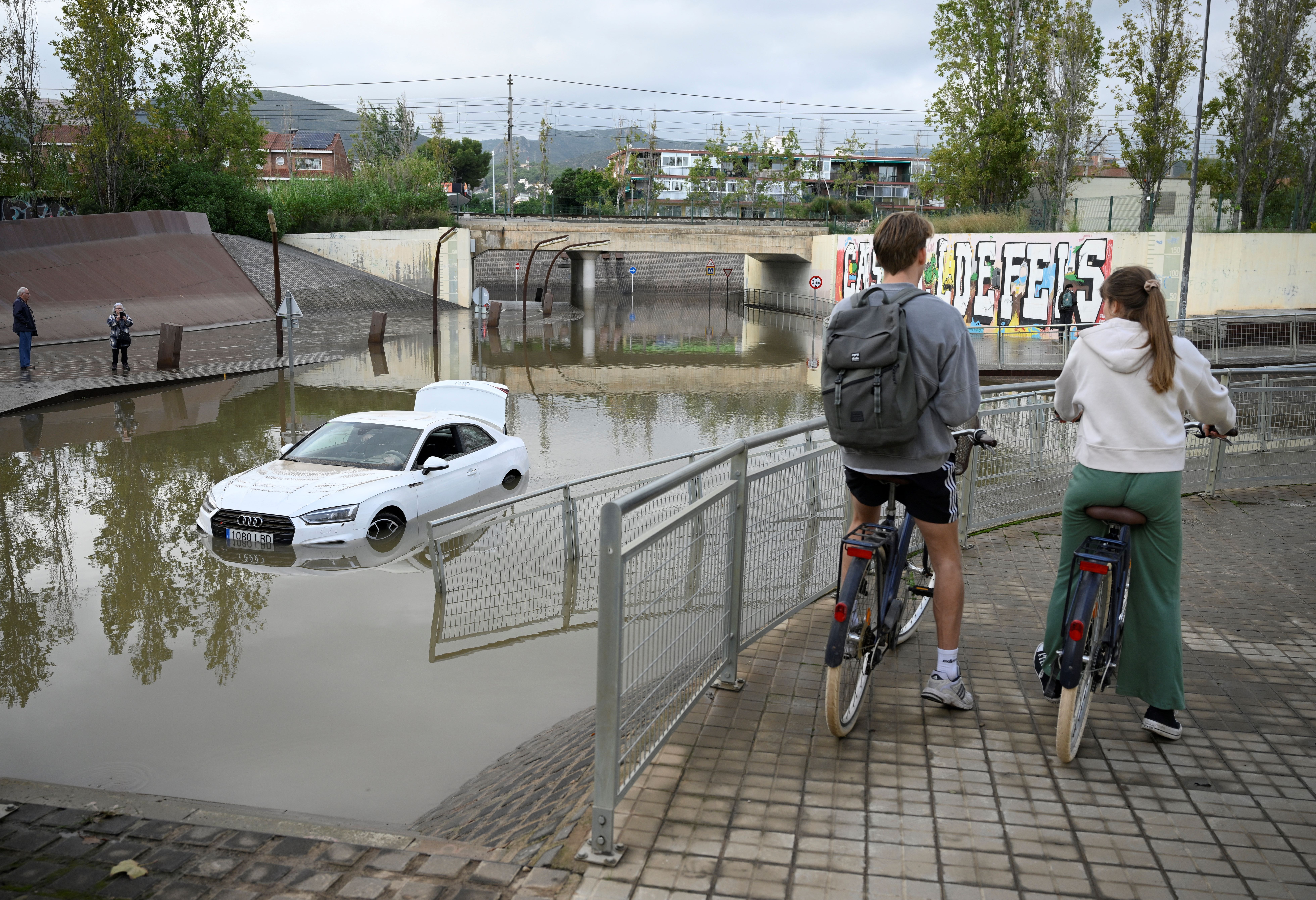 Ciclistas observam um carro inundado nos sub&uacute;rbios de Castelldefels, em Barcelona/Foto: Josep LAGO / AFP