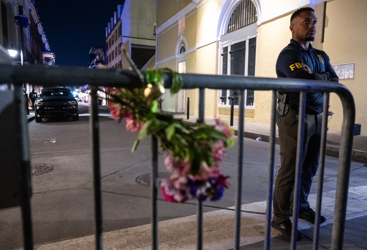 Membro do FBI observa perto de um buqu&ecirc; de flores amarrado a uma cerca, a um quarteir&atilde;o da Bourbon Street, depois que pelo menos 15 pessoas foram mortas durante um ataque na madrugada de 1&ordm; de janeiro de 2025 em Nova Orleans/Foto: ANDREW CABALLERO-REYNOLDS/AFP