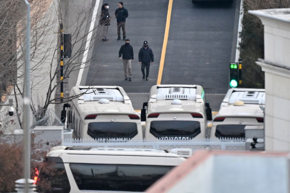 Equipe de seguran&ccedil;a caminha em uma estrada alinhada com &ocirc;nibus bloqueando o port&atilde;o de entrada para proteger o presidente sul-coreano Yoon Suk Yeol/Foto: JUNG YEON-JE/AFP