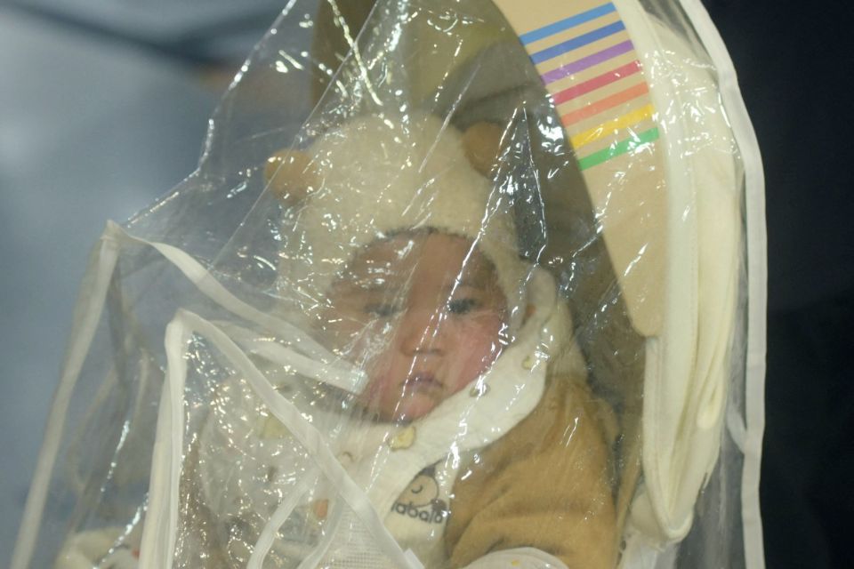 Crian&ccedil;a &eacute; vista atr&aacute;s de uma lona pl&aacute;stica cobrindo um carrinho de beb&ecirc; enquanto espera atendimento no departamento pedi&aacute;trico de um hospital/Foto: STR/AFP