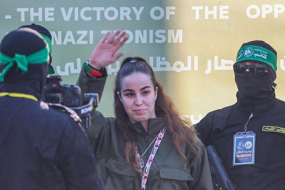 Ref&eacute;m israelense Agam Berger acena enquanto militantes do Hamas a escoltam em um palco antes de entreg&aacute;-la a uma equipe da Cruz Vermelha/Foto: Omar AL-QATTAA/AFP