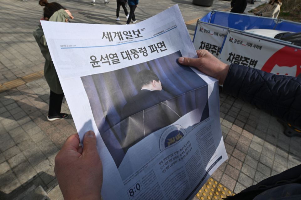 Homem olha para uma edição extra de jornal no centro de Seul depois que o Tribunal Constitucional confirmou o impeachment do presidente sul-coreano Yoon Suk Yeol/Foto: Jung Yeon-je/AFP