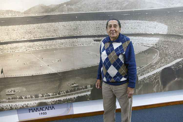 Ghiggia posa em frente ao painel com foto do histórico jogo entre Brasil e Uruguai, no Maracanã 