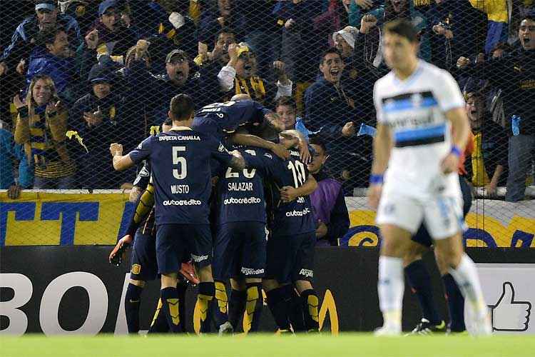 Jogadores do Rosario festejam, enquanto Giuliano caminha desolado pelo gramado no Gigante de Arroyito